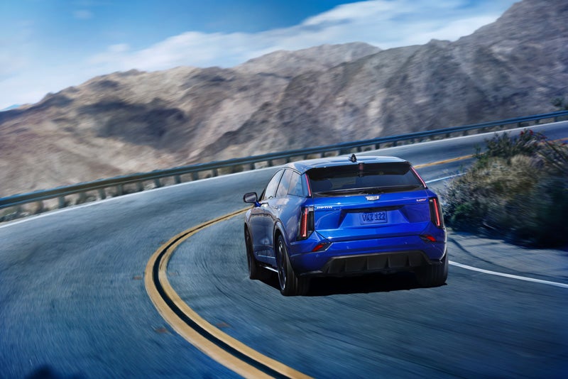 Rear View of a Blue 2026 OPTIQ-V Driving on a Curve of a Mountain Row | Spearfish Cadillac in Spearfish SD